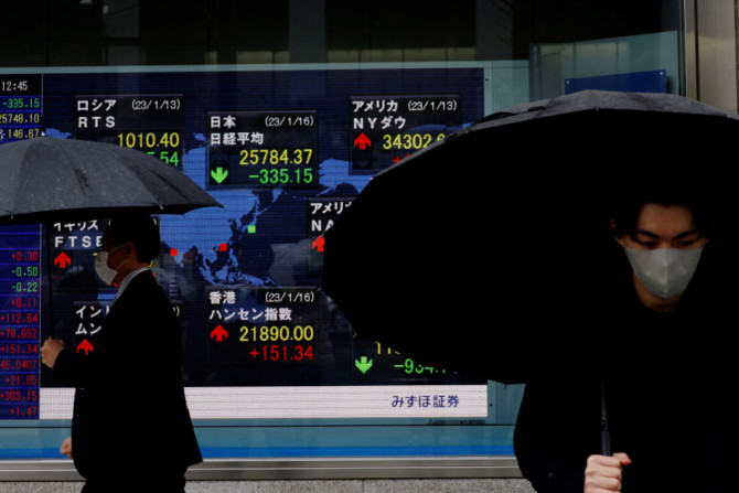 Des hommes passent devant un tableau électrique affichant les indices Nikkei et d&#39;autres pays devant une maison de courtage à Tokyo