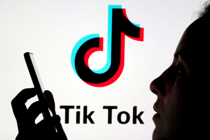 Une personne tient un smartphone alors que le logo Tik Tok est affiché derrière dans cette illustration