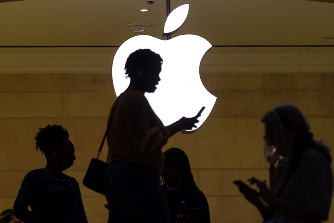 une femme utilise son appareil mobile iPhone alors qu&#39;elle passe devant un logo Apple illuminé dans l&#39;Apple Store de New York